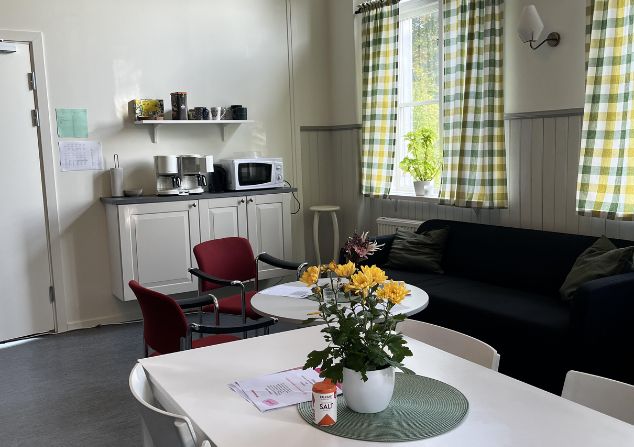 Ett rum med bord och stolar med blommor på bordet och en bänk med microvågs ugn och kaffebryggare på.